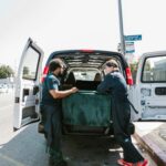 Two movers load a van with furniture during moving day.