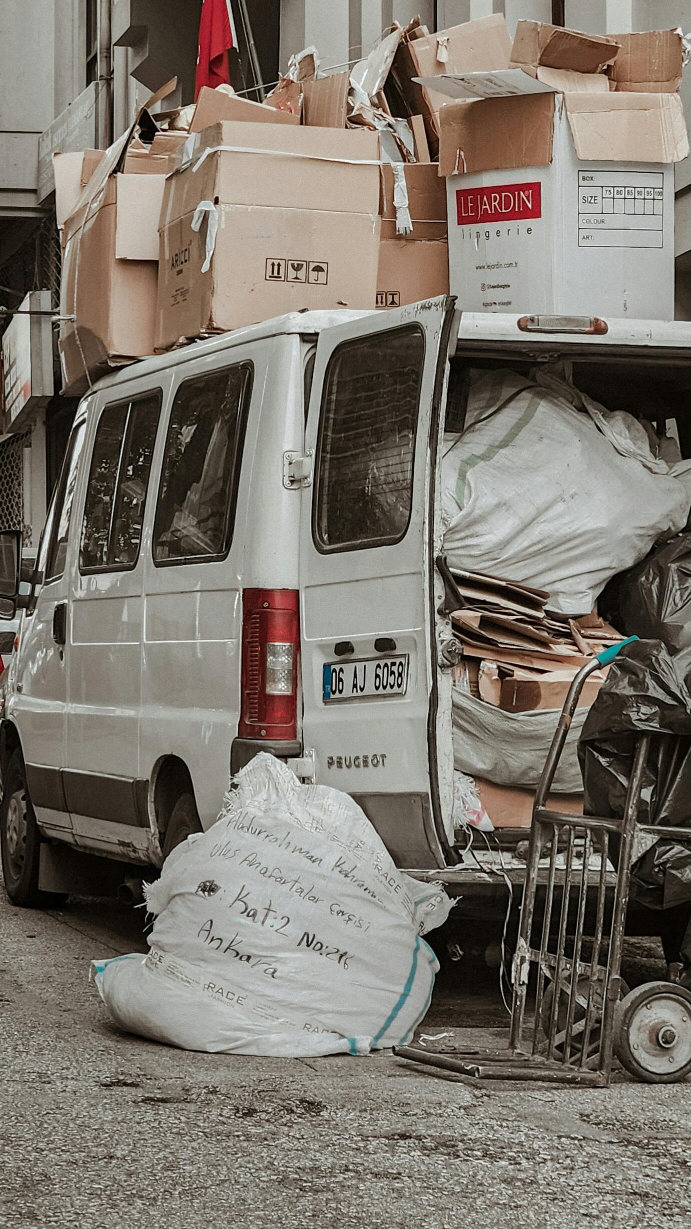 A white van loaded with cardboard boxes and bags in a crowded alleyway, illustrating urban storage challenges.